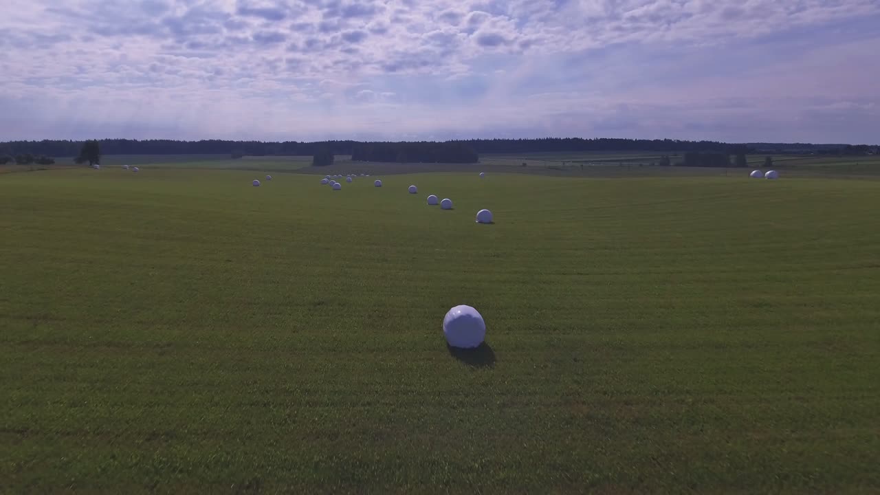 Aerial Dolly In Drone Shot Of Flying Forward Above White Hay Rolls