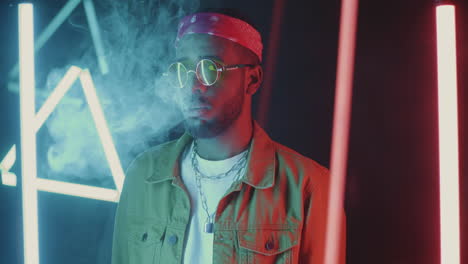 stylish man exhaling smoke in neon lights