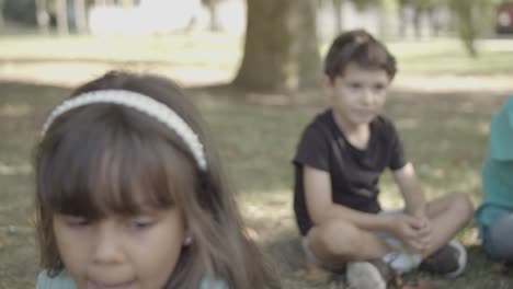 Latin-long-haired-girl-sitting-on-grass-in-the-park-and-holding-paper-fan