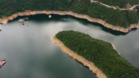 volando cerca de la curva del embalse de vacha rodeado de árboles del bosque y pequeñas casas en el agua