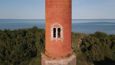 ascending flight up along a old lost place lighthouse without windows and old roof at the coast of baltic sea - estonia in europe - nature helicopter flyover establishing shot summer 2022 - bird view