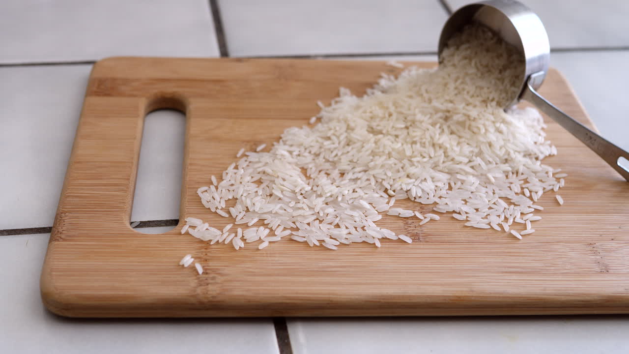 un montón de granos de arroz blanco saliendo de una taza medidora en una cocina para una receta a base de plantas deslice hacia la derecha
