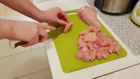 mujer caucásica cocinando y cortando carne de pechuga de pollo cruda