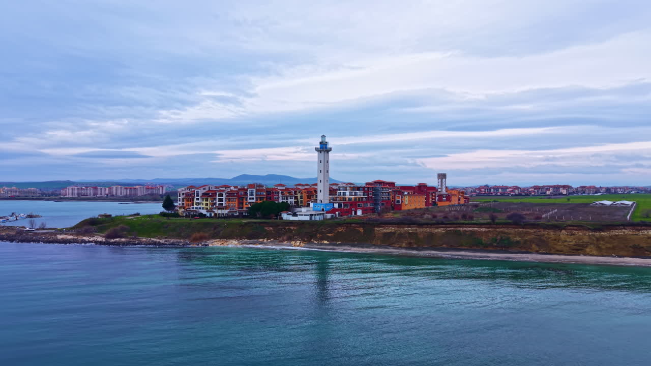 Vista costiera con un faro ed edifici vicino alla riva in un porto tranquillo durante il giorno con nuvole variabili