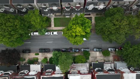 tracking shot of white car driving down quaint suburban street lined with townhomes, parked cars, and trees