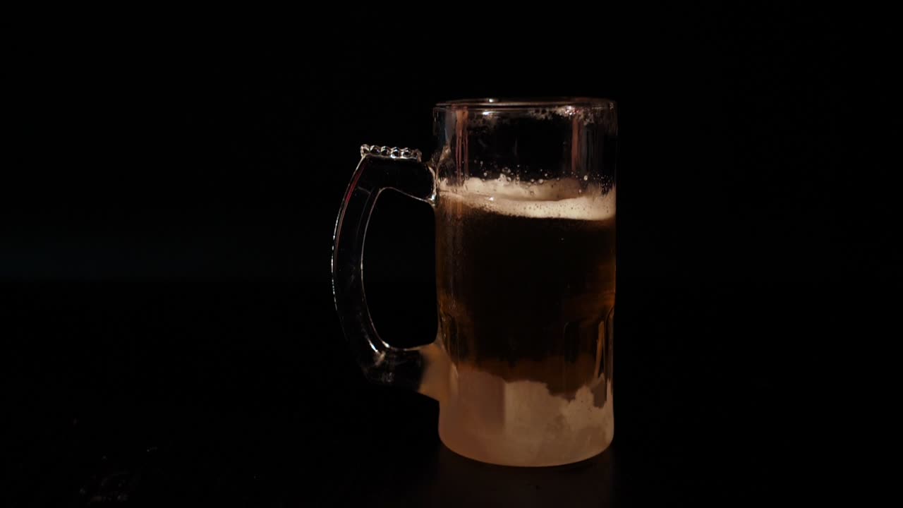 Una mano posa un boccale ghiacciato di birra fredda su sfondo scuro