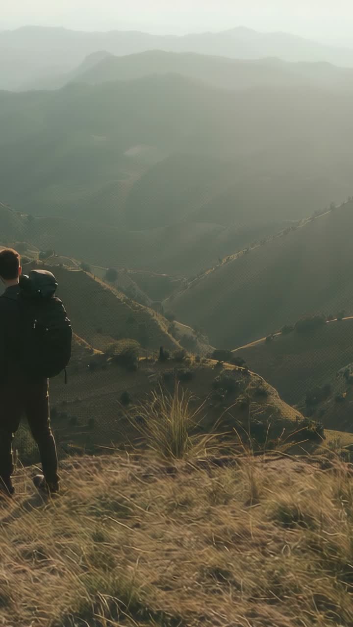 Vertical video: Reaching ridge, solo hiker in dark coat scanning valley for route, pack, copy space