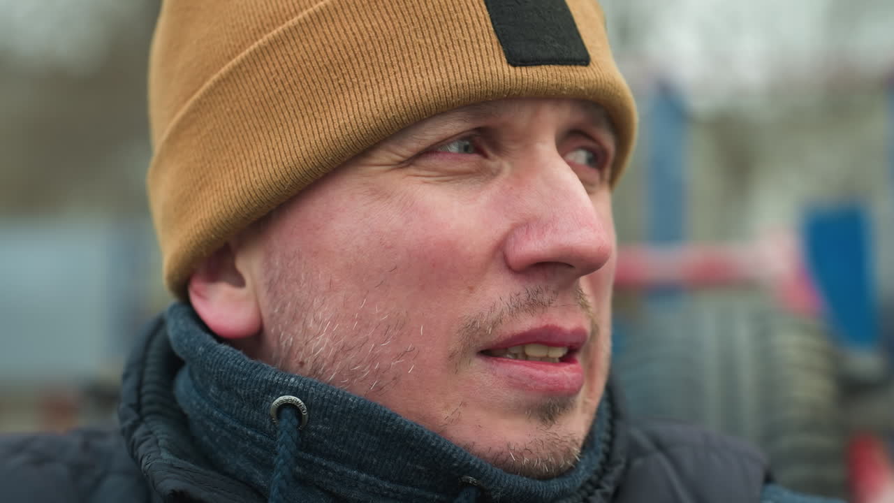 Close-up of a coach sitting on workout equipment, looking tired and adjusting his jacket collar with his hands