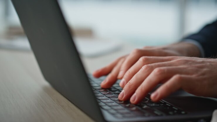 Nahaufnahme: Hände eines Geschäftsmannes tippen auf Laptop-Tastatur im modernen Büro.