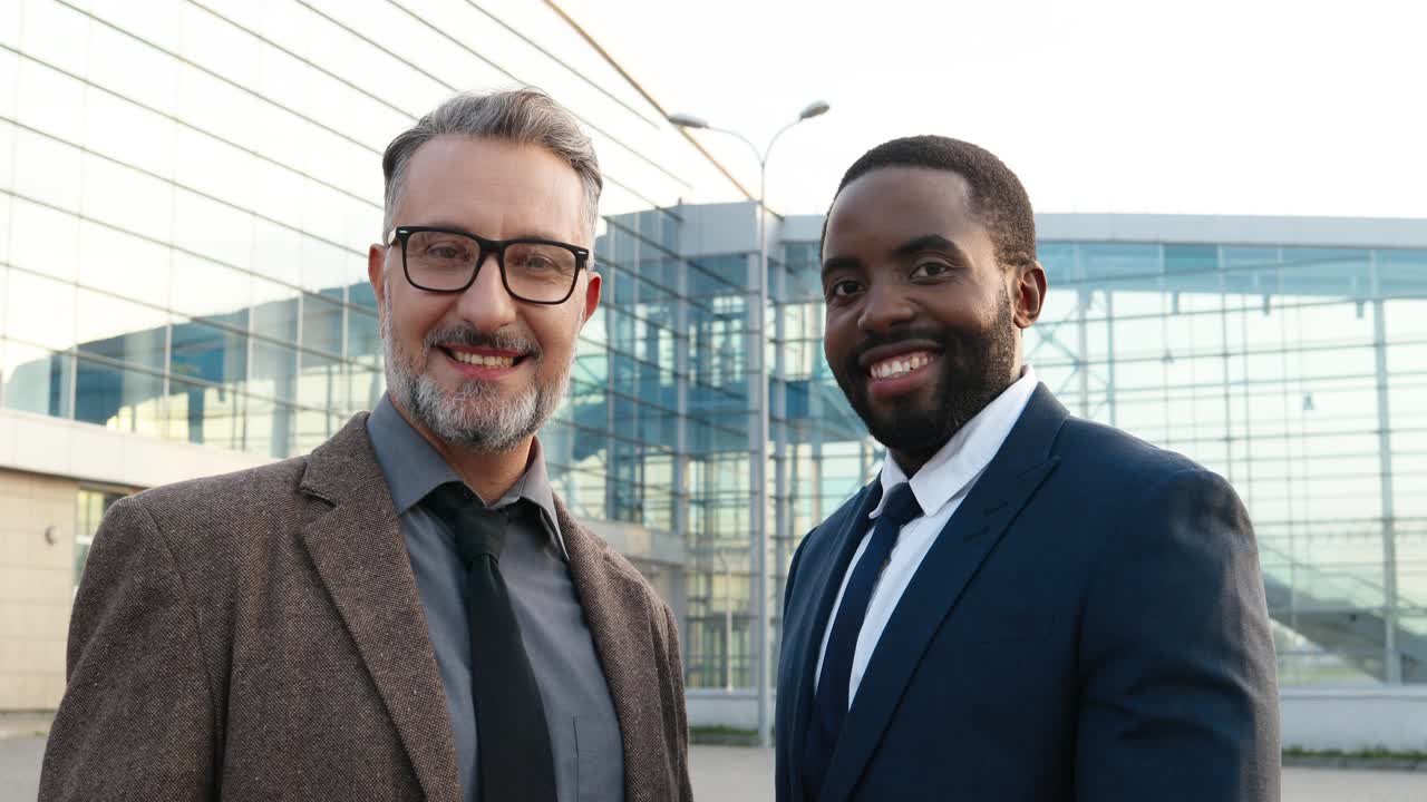 Close-up view of cheerful caucasian and african american businessmen smiling at camera in the street