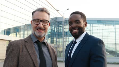 vista cercana de alegres hombres de negocios caucásicos y afroamericanos sonriendo a la cámara en la calle