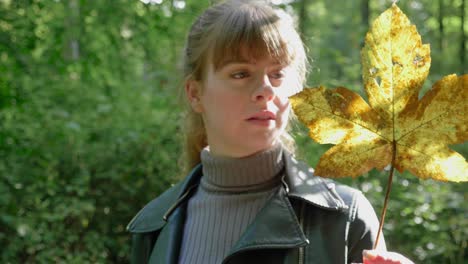 girl stares in wide-eyed wonder at golden leaf in sunlit woods, close-up