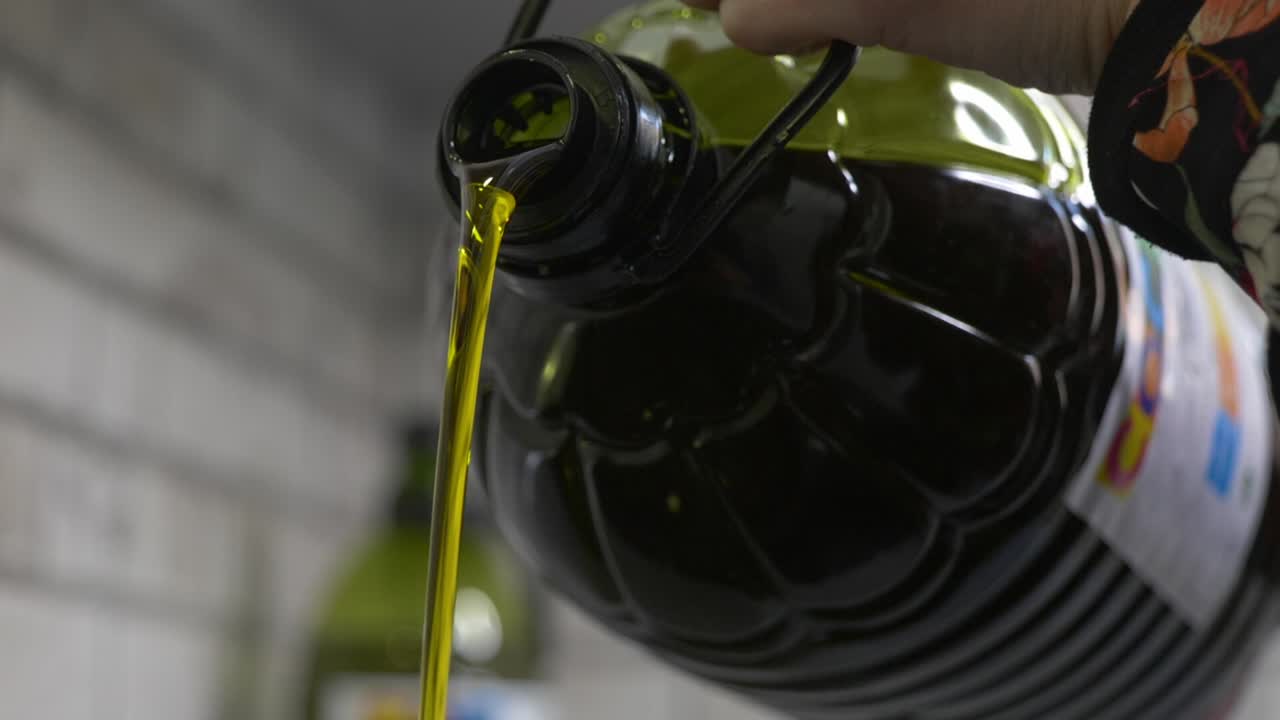 A flow of Extra Virgin Olive Oil (EVOO) being poured from a jug. The golden color and silky texture highlight the quality of the product, essential in the Mediterranean diet