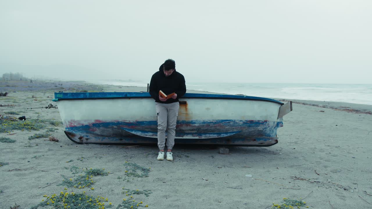 Man Reads A Book In Solitude By The Sea On A Gloomy Day