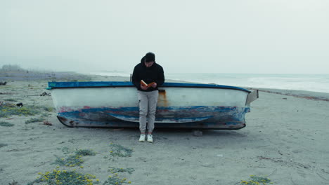 man reads a book in solitude by the sea on a gloomy day