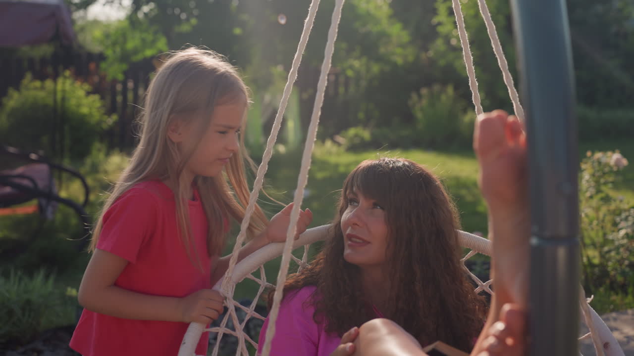 Serene Garden Moment With Loved Ones Present, Quiet Summer Day Spent With Family In Vibrant Outdoor Setting, Peaceful Scene Of Mother And Daughter Relaxing In Lush Garden During Sunny Afternoon