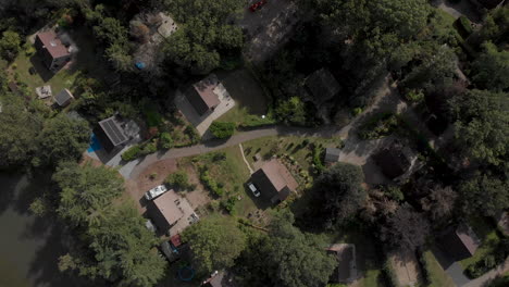 Top-down-aerial-approach-of-a-summer-house-recreational-park-with-a-small-pond-and-meandering-path-in-green-surroundings