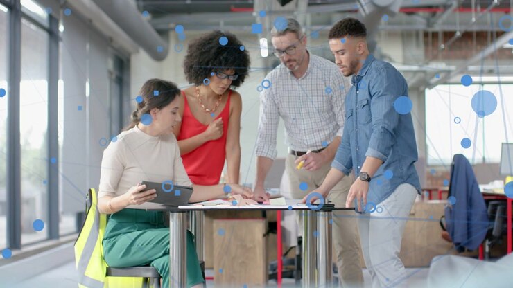 Four colleagues tapping tablet, pointing at paperwork and pens, animated overlays guiding design