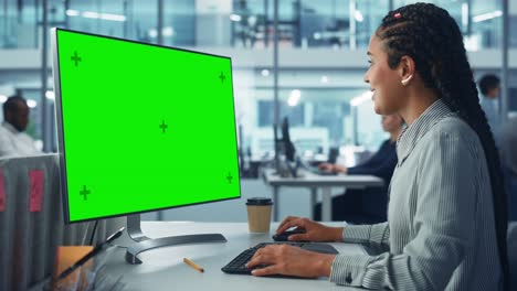 oficina corporativa: técnica informática negra que utiliza una computadora de escritorio con pantalla clave de croma verde. ingeniero de software creativo sonriente que trabaja en el marketing, el desarrollo y el proyecto de comercio electrónico.