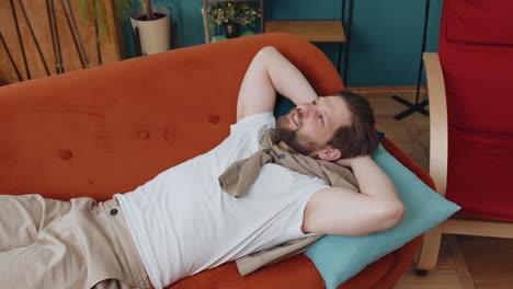 tired young man lying down on comfortable couch, taking a rest, daytime nap relaxing falling asleep