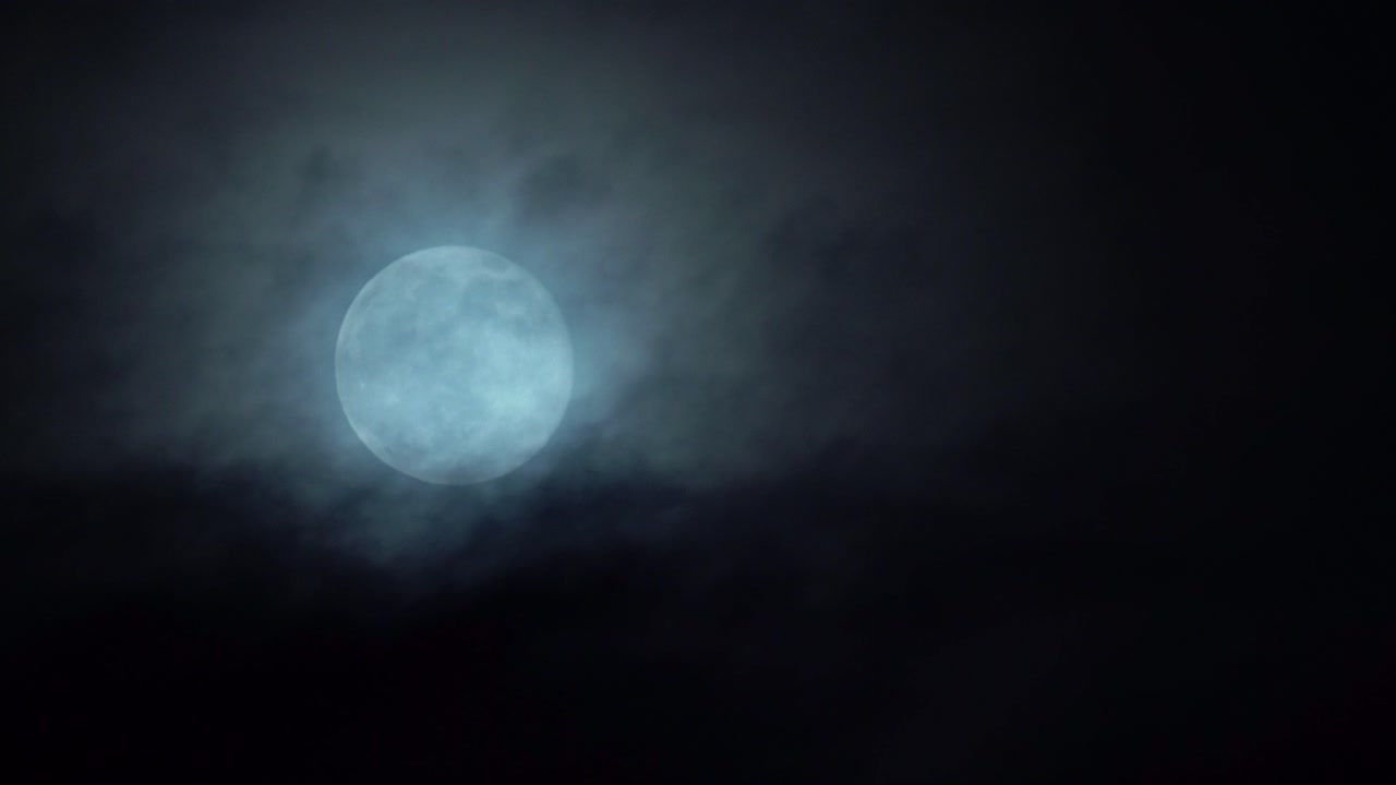 Bright white full moon rising in the sky - Dark mystical clouds passing in front while moon slowly moving upwards in frame