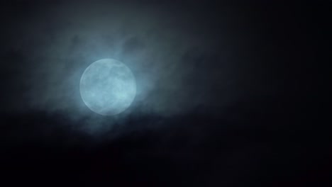 bright white full moon rising in the sky - dark mystical clouds passing in front while moon slowly moving upwards in frame