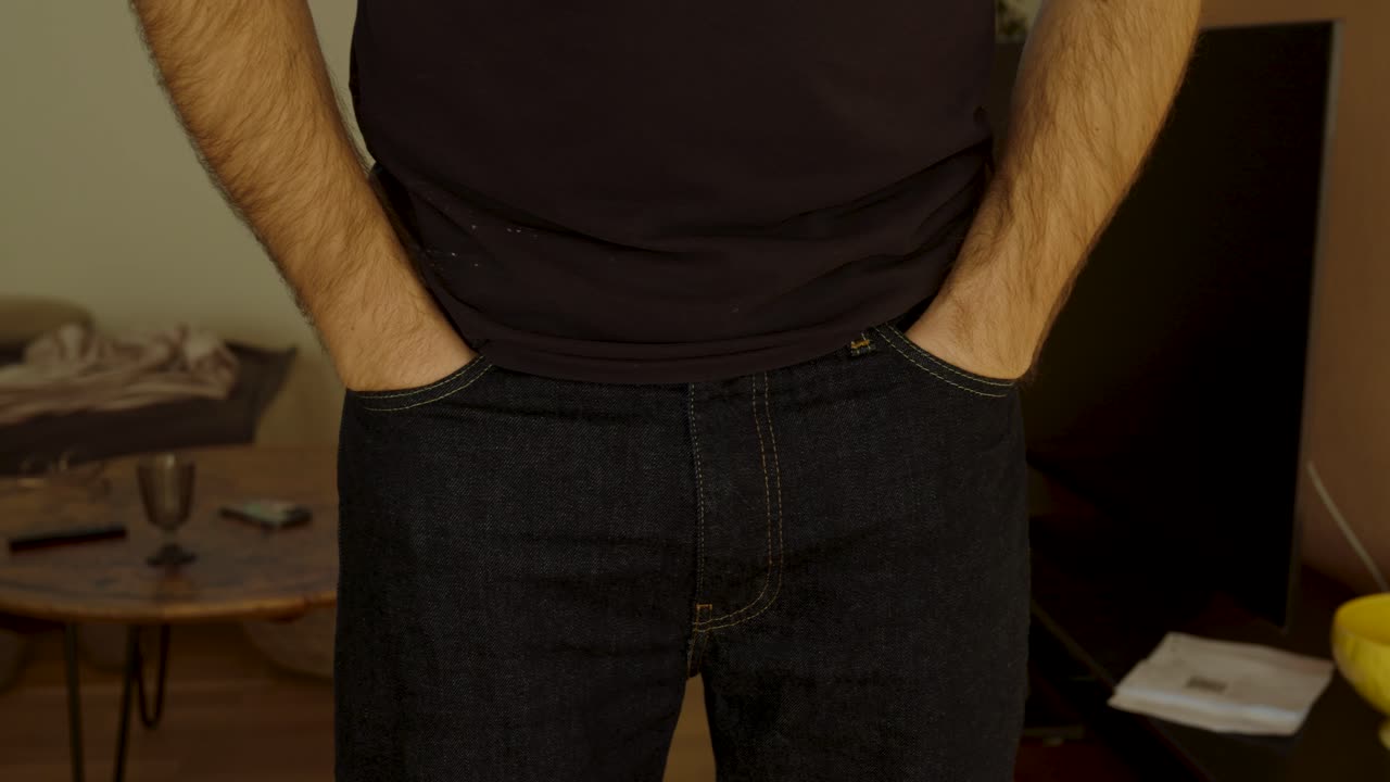Inquadratura cinematografica a mezzo busto di un uomo che mostra diverse posizioni neutre in piedi (mani in tasca, mani sui fianchi e mani giunte), utili per concetti di comunicazione e linguaggio del corpo nella vita quotidiana.