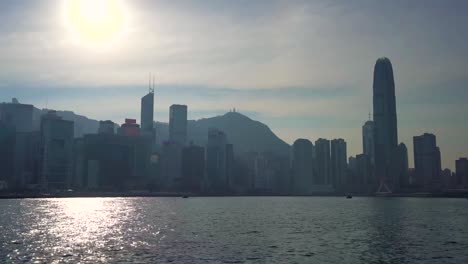 Beautiful-famous-Hong-Kong-Mega-City-Skyline-silhouette,-sailing-across-Victoria-Sea-Harbor-on-a-boat-on-Hot-Sunny-Blue-Sky-Summer-Day,-bright-sun-shining-reflecting-on-water