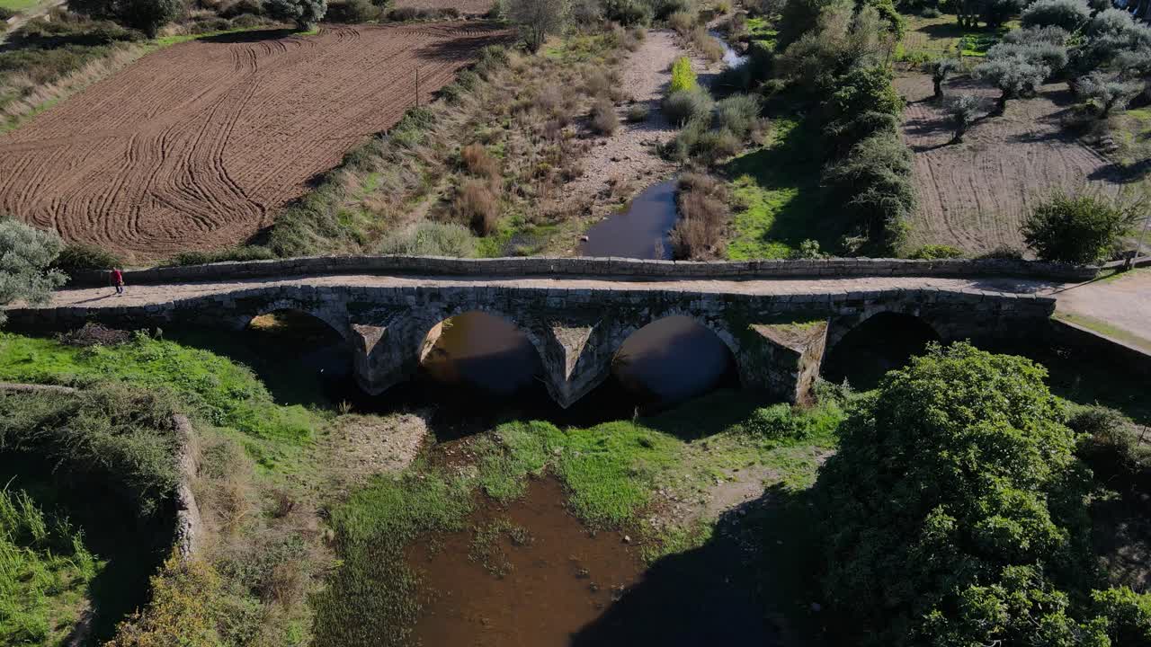 drone se eleva sobre el puente romano idanha-a-velha mientras un peatón cruza