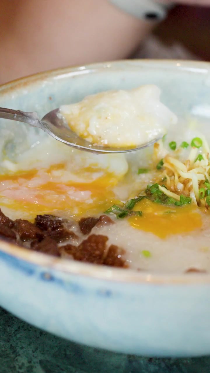 Tangkapan dekat sendok menyendok bubur nasi gurih dengan telur dan hiasan jahe