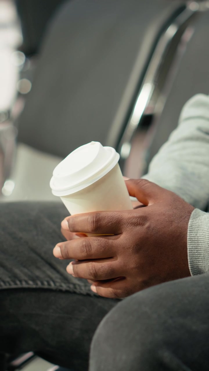 Persona che tiene in mano una tazza di caffè usa e getta mentre è seduta