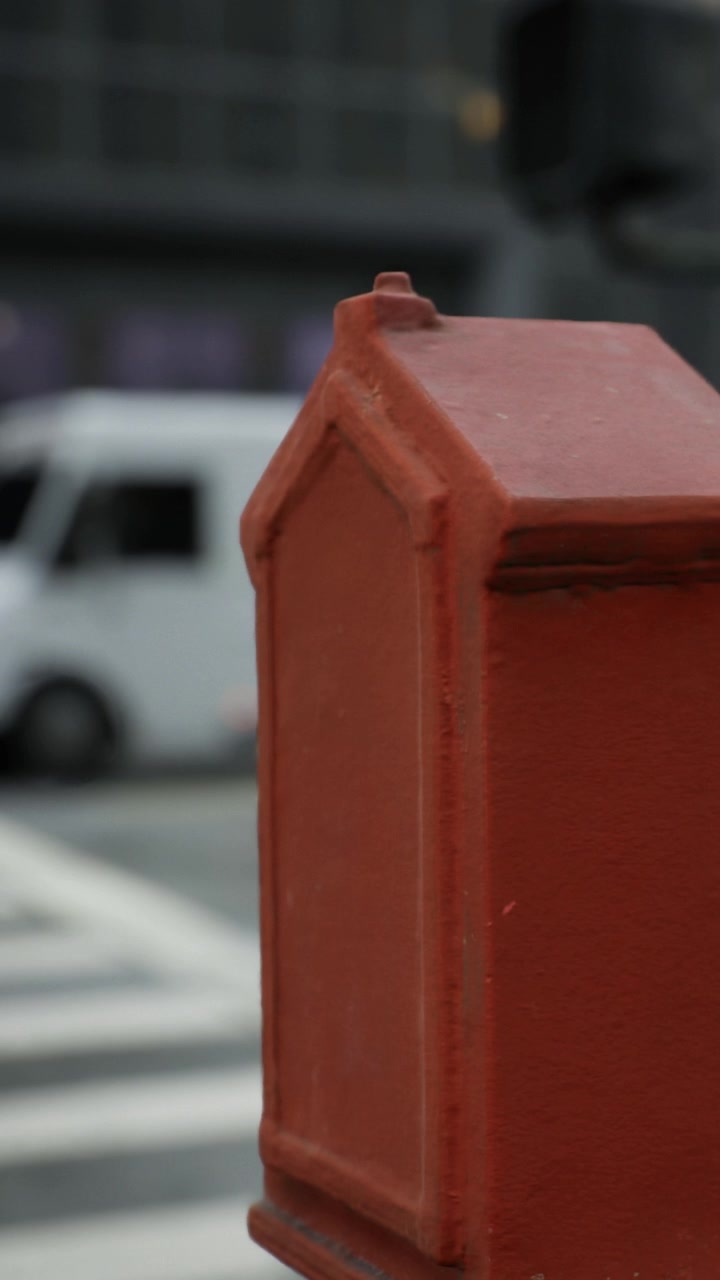 Una cassetta delle lettere rossa si trova all'angolo della strada mentre le persone camminano dietro di essa in città