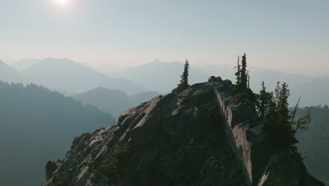 imágenes aéreas que giran alrededor de la cima del pico de una montaña que está cubierta de árboles y rocas