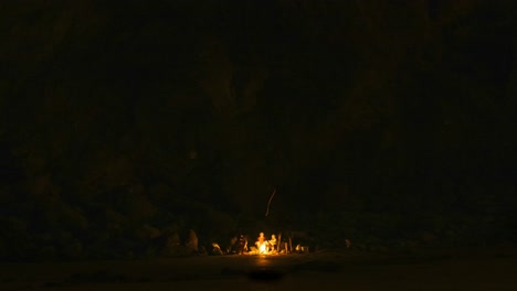 group sitting around bonfire in the dark. outdoor social gathering of friends on beach.