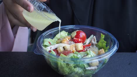 a woman pouring dressing on a salad