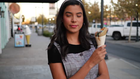 a cute young hispanic woman holding an ice cream cone and smiling with happiness at a dessert shop on a city street slow motion