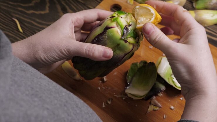 Woman cleaning artichokes. Dropping lemon drops. Cooking process at the kitchen. Closeup