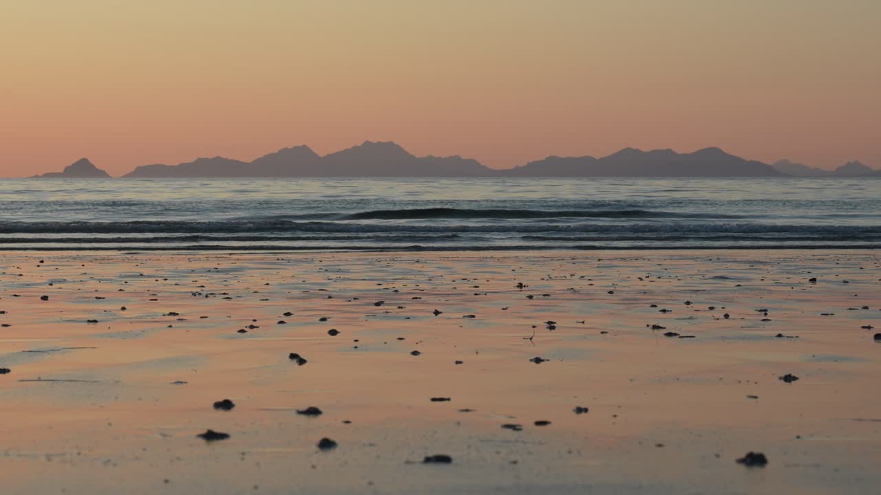 A breathtaking sunset bathes the ocean in warm hues, with gentle waves and silhouetted islands and mountains on the horizon. Perfect for cinematic and nature videos