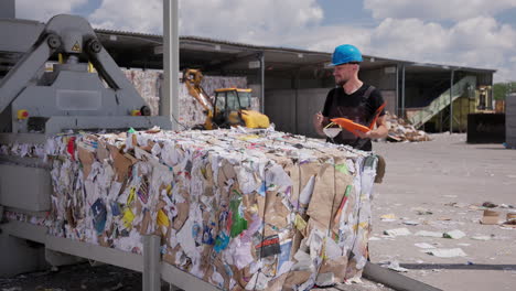 Worker-takes-notes-by-paper-bale-at-outdoor-recycling-facility,-slomo