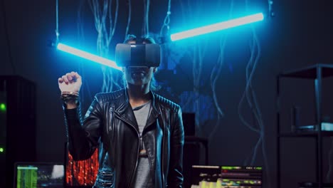 young woman in vr glasses scrolling and tapping in the air with her hands while having vr headset in the dark room with neon lights, wires and computers