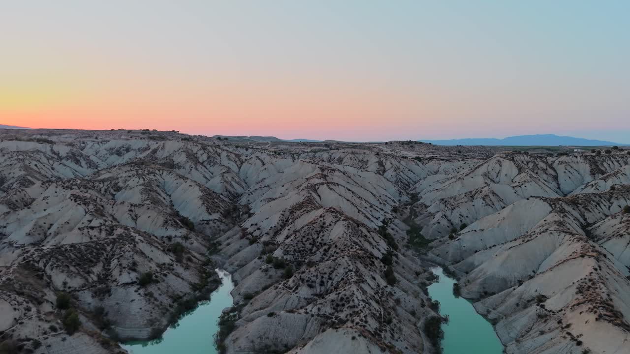 Aerial view of a desert landscape with gullies and a reservoir at sunset