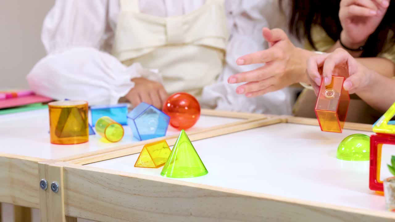 Kids and teacher interact with translucent geometric blocks on a bright classroom table, natural lighting