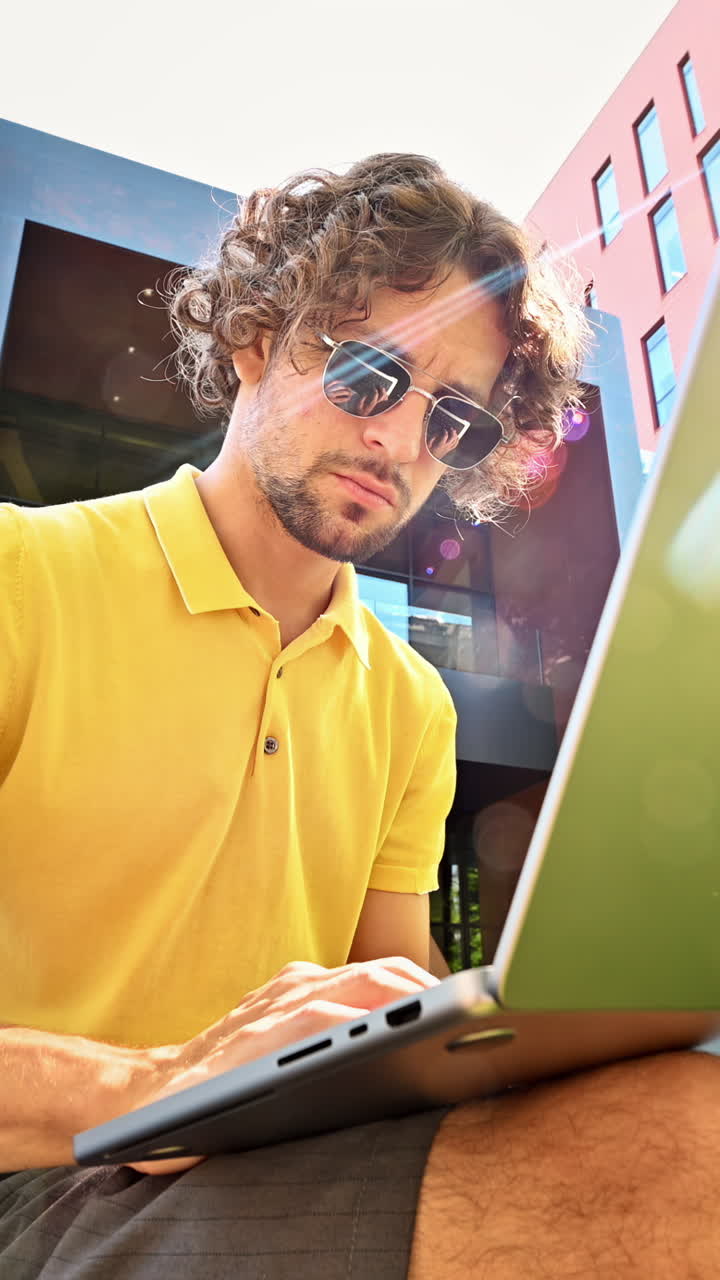 Man in yellow shirt talking standing on a bench and working on a laptop. Vertical