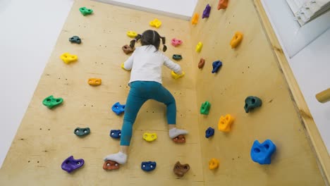 wide shot of a fearless little girl climbing an indoor rock climbing wall