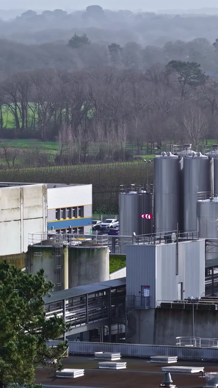 Industrial storage silos surrounded by forest and rural landscape on hazy day, vertical