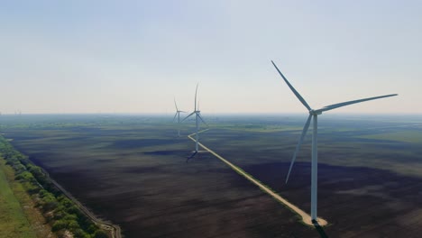 wide-shot-of-the-Texas-San-Roman-wind-park,-aerial-shot,-wind-turbines,-wind-power-station,-farmland,-drone,-wind-farm,-sunny-day,-blue-sky,-hazy-morning,-aerial-flight,-flying-pov