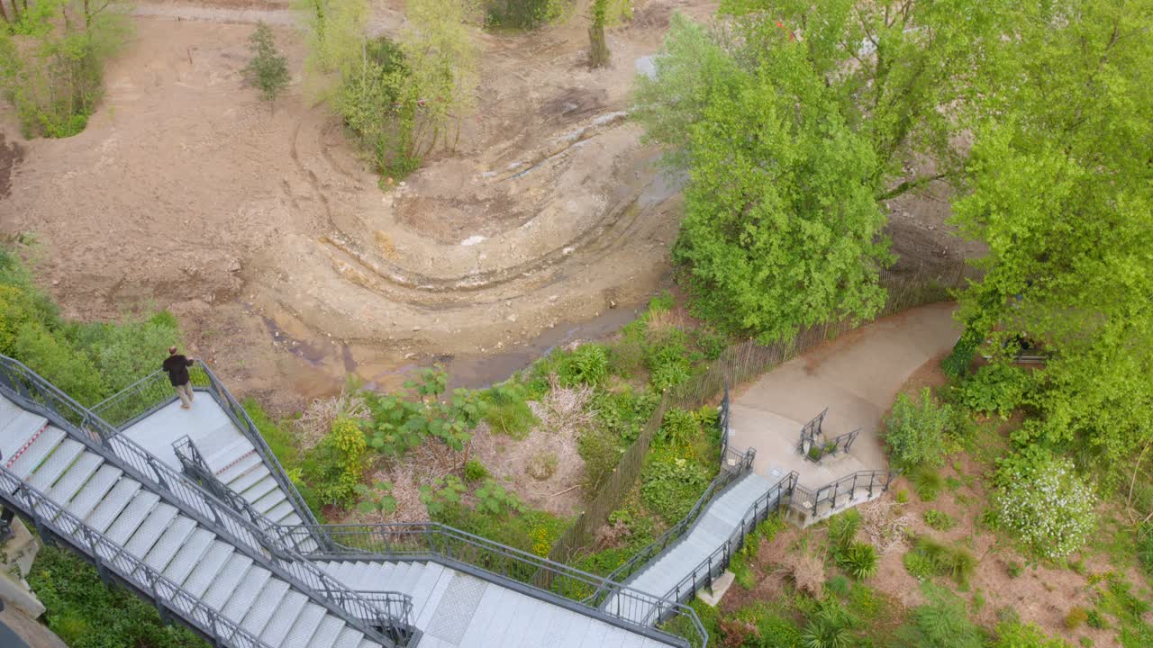 Person on a large outdoor metal staircase overlooking a dry riverbed and park