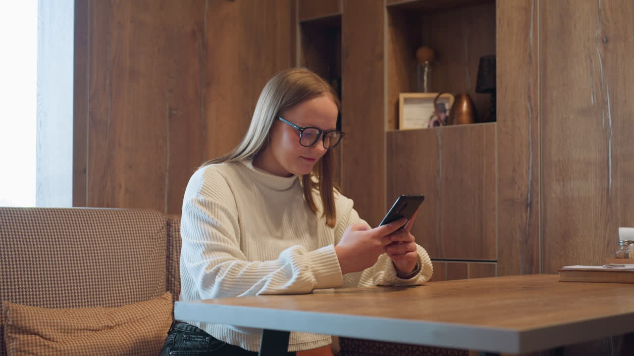 cheerful woman in white sweater smiling warmly while looking at smartphone and enjoying heartfelt conversation with husband in cozy modern interior with wooden decor and soft ambient light
