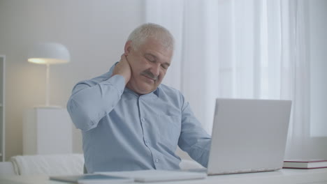 hombre de mediana edad con osteocondrosis del cuello está trabajando con una computadora portátil dolor por el esfuerzo excesivo de los músculos masajeándose para relajarse