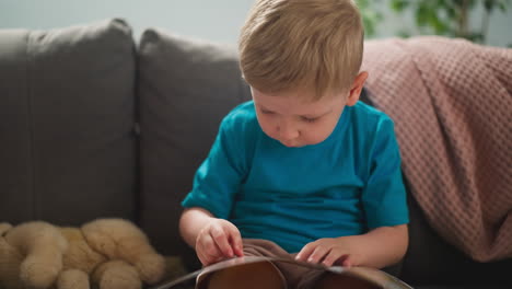 Concentrated-little-boy-looks-at-pictures-sitting-on-sofa